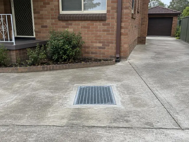Outdoor driveway drain grate beside a brick house and driveway in Wentworthville