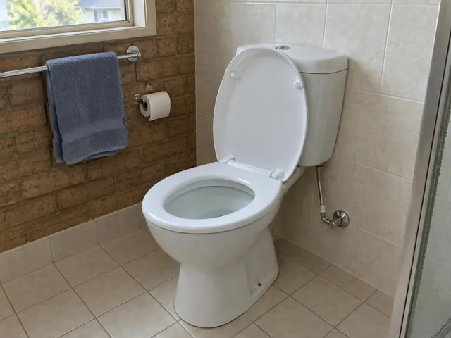Clean white toilet in a tiled bathroom with towel rail and brick wall in Seven Hills