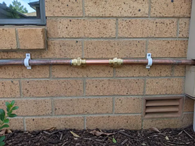 Repaired copper water pipe on a brick exterior wall with pipe clips in Toongabbie